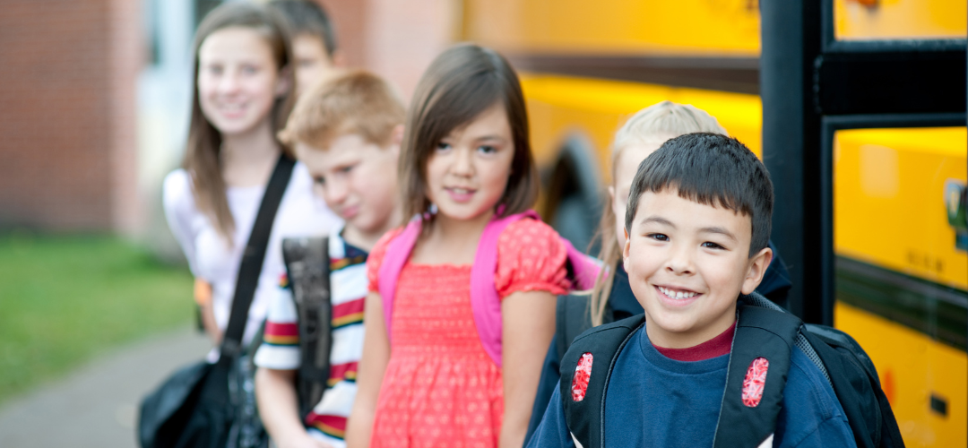 An image of kids going back to school in front of a bus