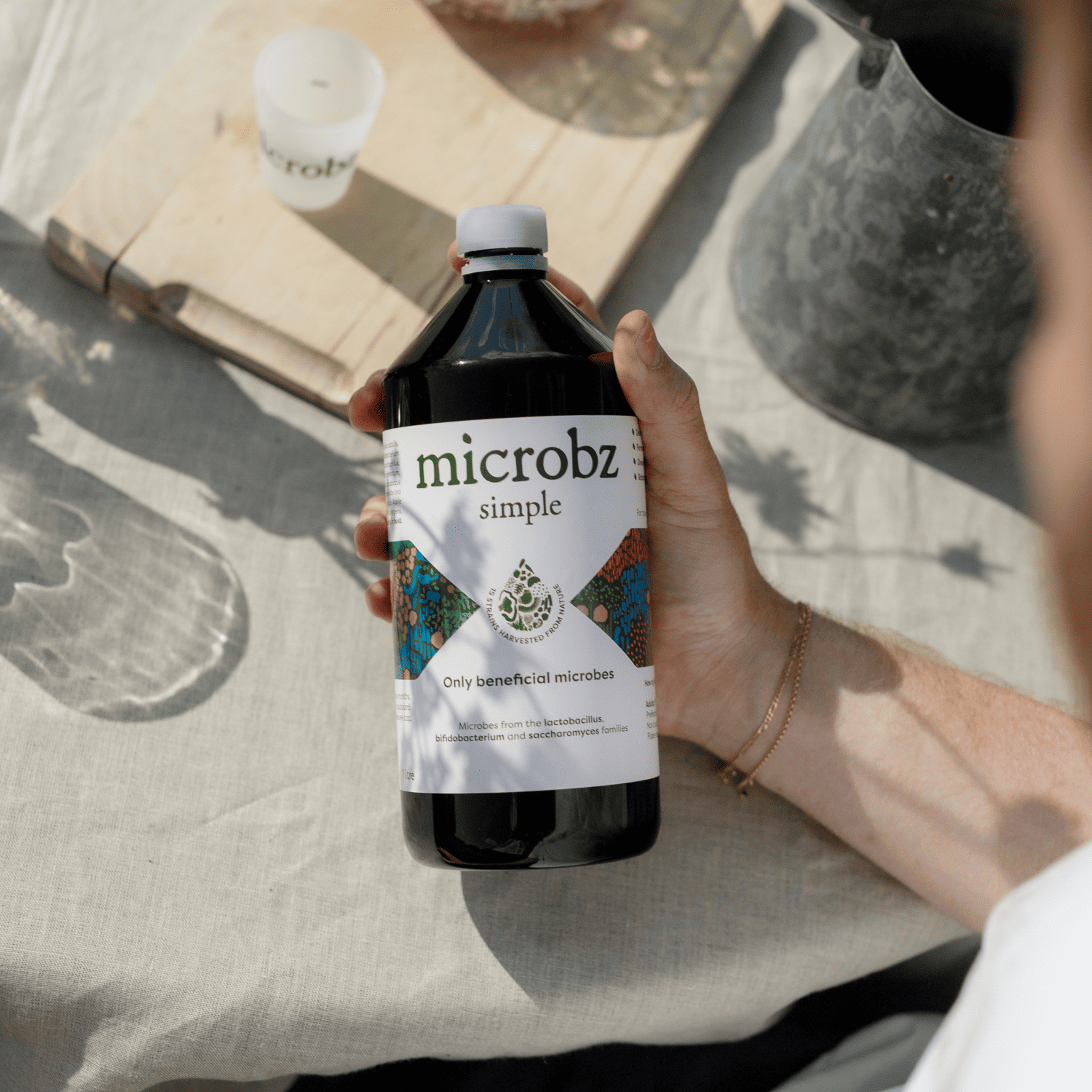 Hand holding a bottle of 'microbz simple' on a textured surface with a blurred background