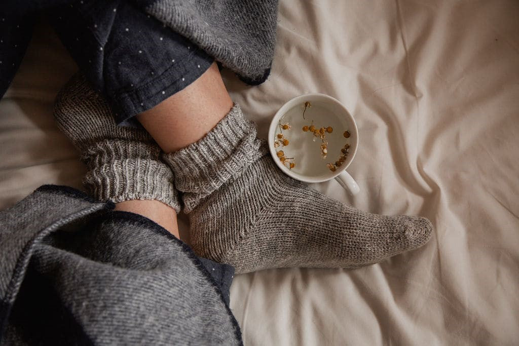 Cosy image of feet with a cup of chamomile tea on the bed