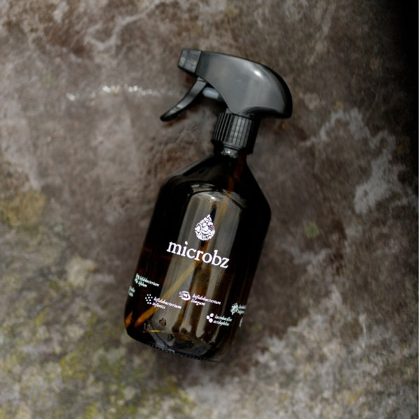 Glass spray bottle with black nozzle labeled 'microbz' on a textured brown background