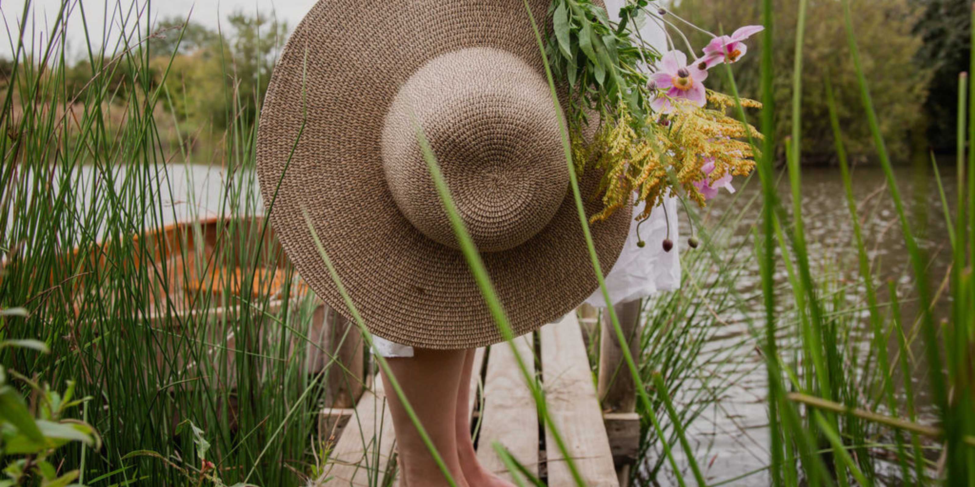 lady and a wooden peer on a lake with a hat and flowers. She has a healthy gut