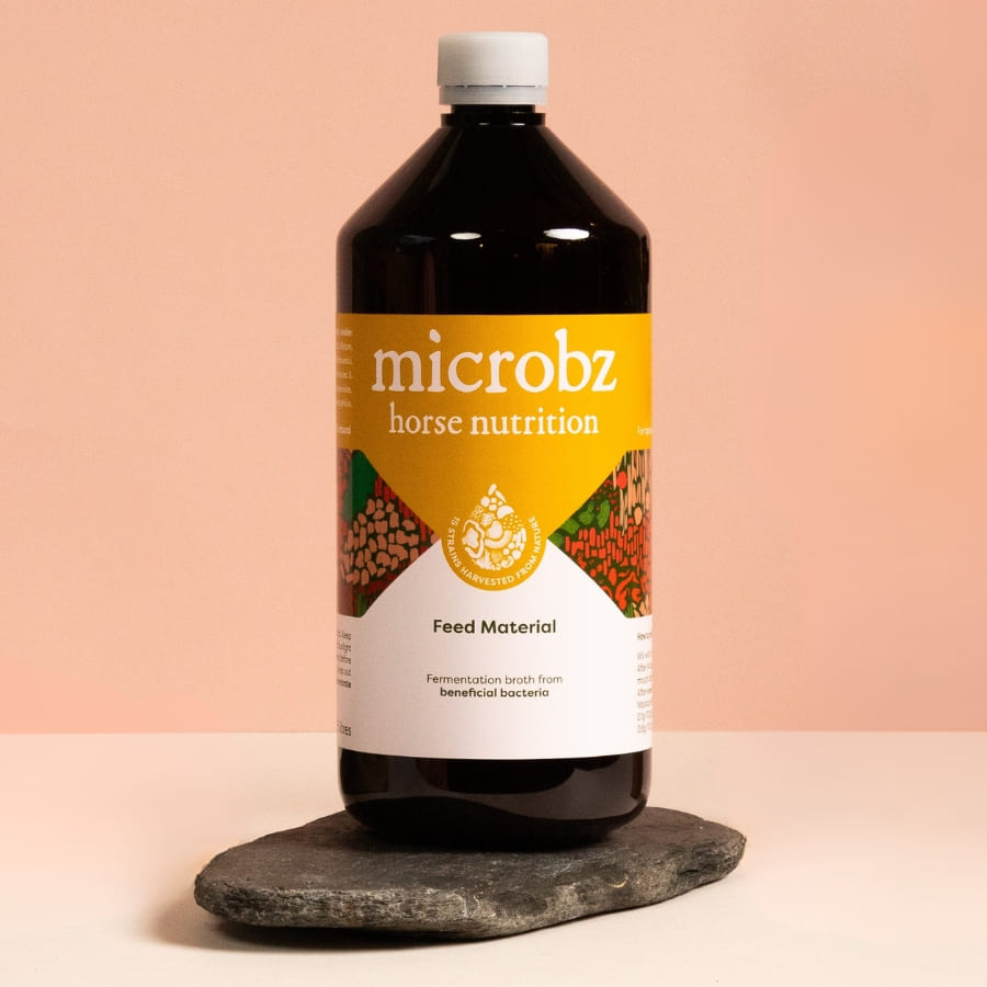 Bottle of microbz horse nutrition a gut supplement for horses on a stone surface with a pink gradient background