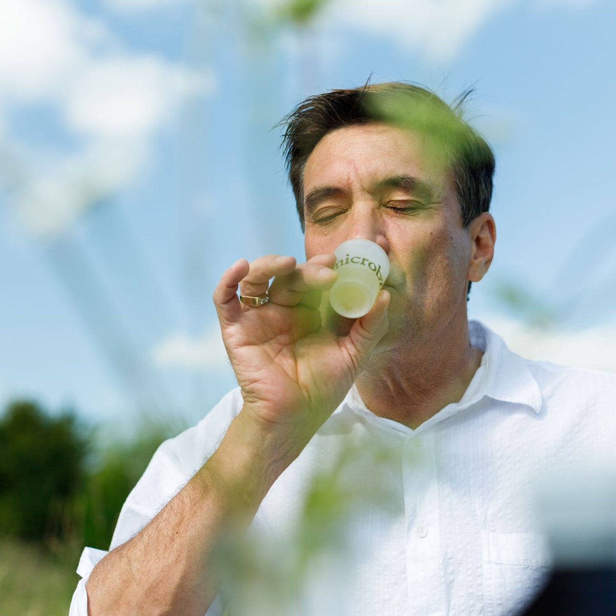 Man holding a small branded microbz shot glass outdoors with a blurred background