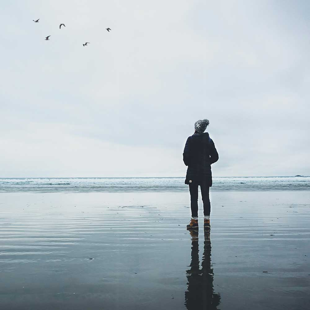 lady on the beach staring in to the sky at some birds thinking about her ibs and bloating