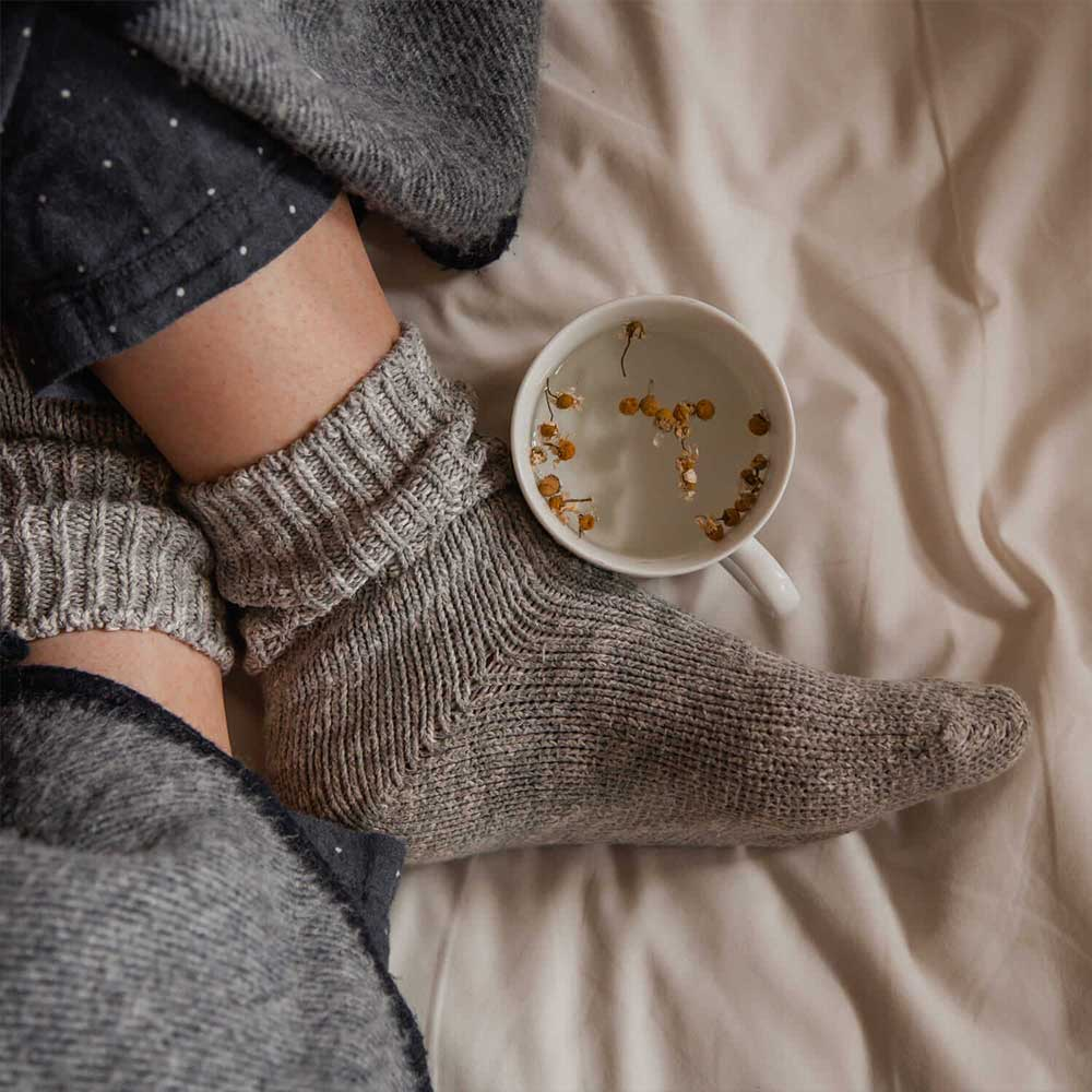 lady feet with comfy socks and a hot cup of herbal water and probiotics for hormonal trouble