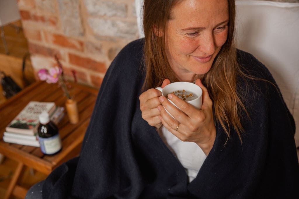 woman smiling whilst taking Bio-Live Breathease probiotic to help with immune system and sat at the table with sourdough bread and an artichoke