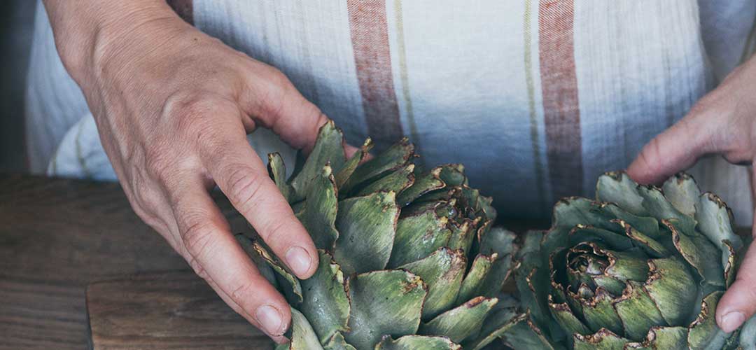 How stress damages gut health: woman holding artichokes on wooden chopping board