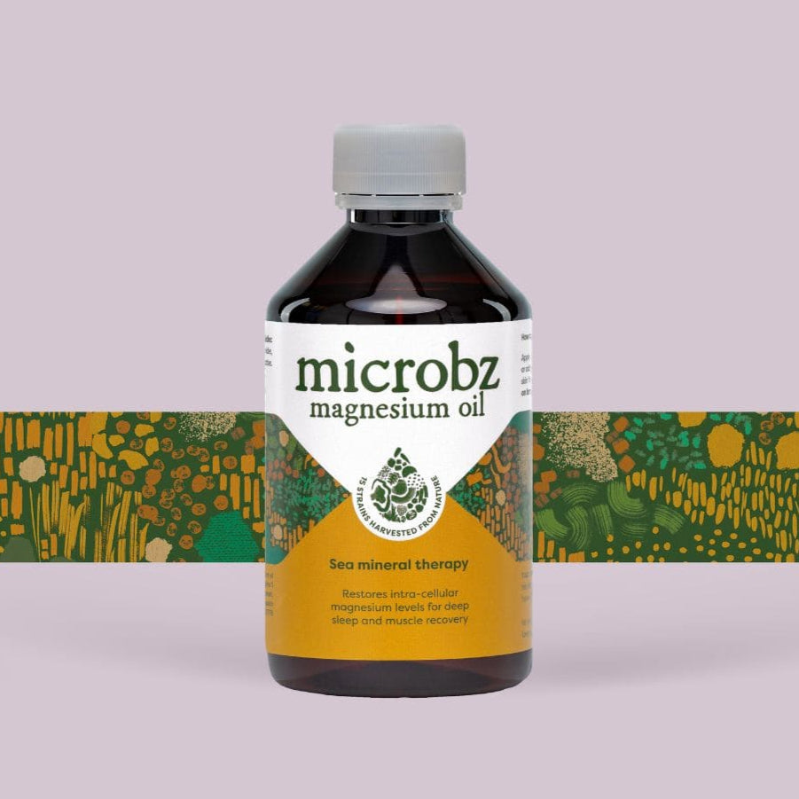 A bottle of Microbz magnesium oil with a green and yellow label, set against a pink background with a floral pattern.