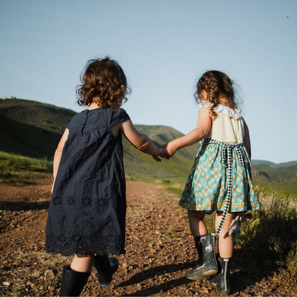 two small girls holding hands going up a hill in nature. They have been using kids probiotics for children and feel back to nature