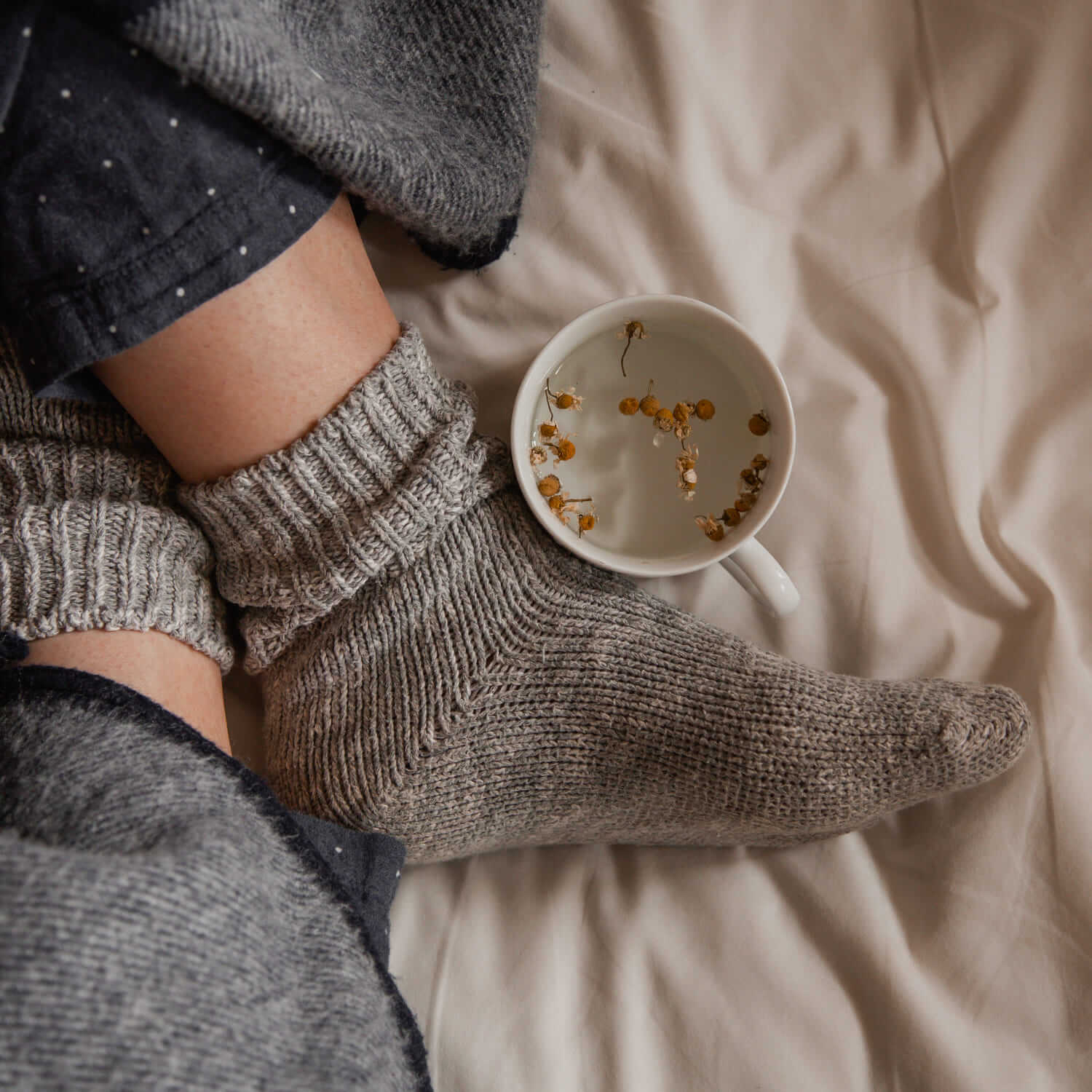 feet with cosy socks on a bed with a cup of chamomile tea